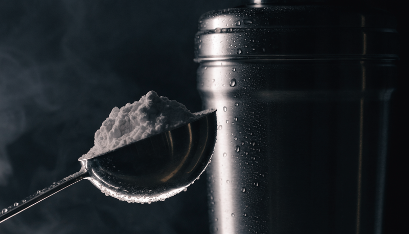 Close-up van creatine poeder scoop naast shakebeker, donkere obsidian studio sfeer