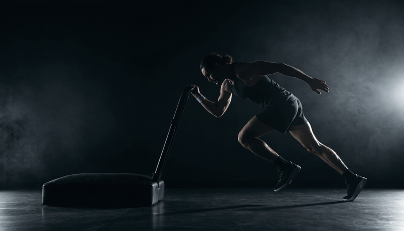 Atleet duwt een sled tijdens functionele fitness training, donkere obsidian studio sfeer met zweet en intensiteit