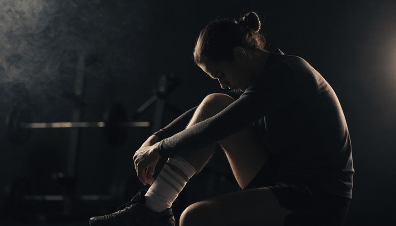 Atleet met bandage om enkel rust naast trainingsmateriaal, donkere obsidian sfeer