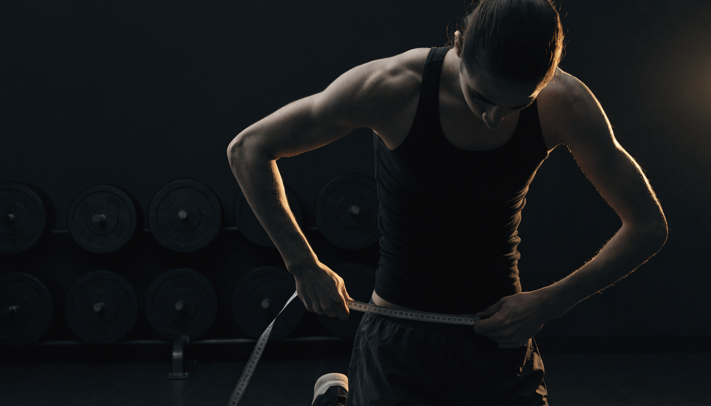 Gespierde atleet meet zijn buikomtrek, donkere obsidian fitness sfeer