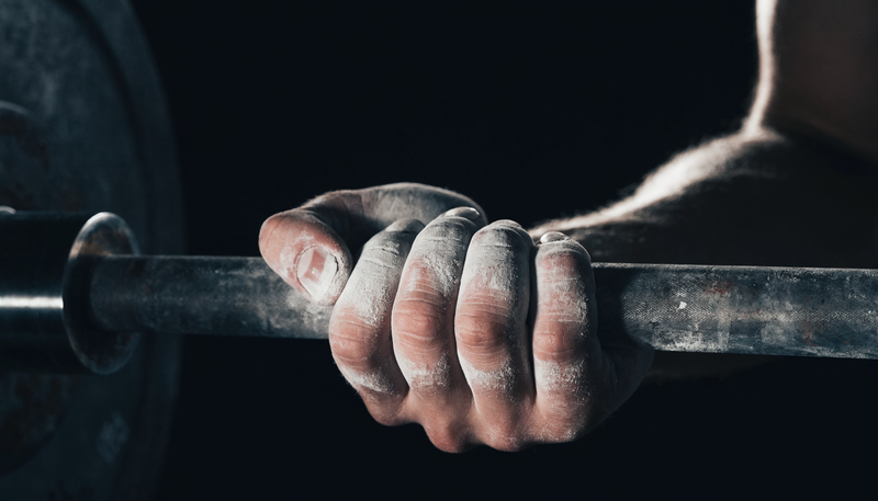 Close-up van een atleet die een zware halterstang vastgrijpt met krijt op de handen, donkere obsidian sfeer