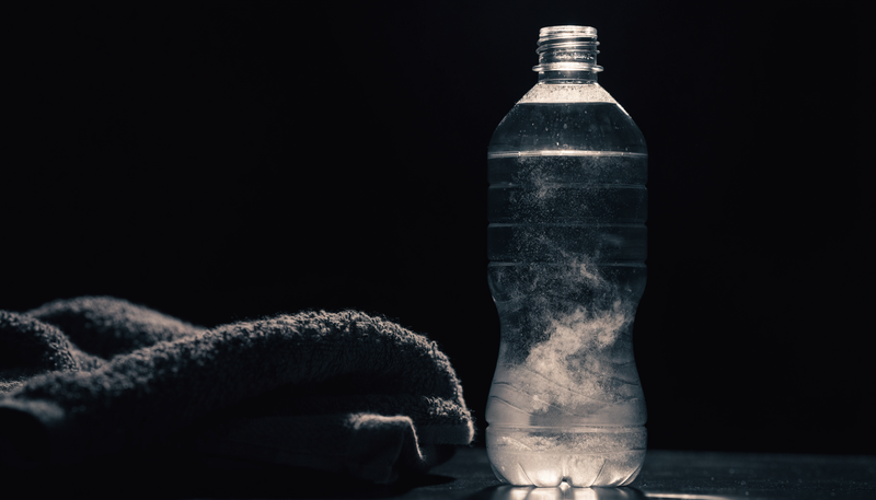 Glas water met elektrolyten poeder en zweet op een handdoek, donkere obsidian studio sfeer